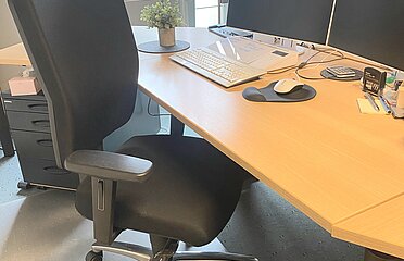 Ein Schreibtisch mit PC und einem Bürostuhl.