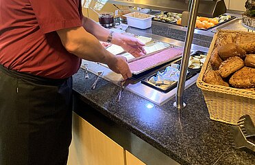 Servicemitarbeiter legt eine Aufschnittplatte in die Büfettauslage.